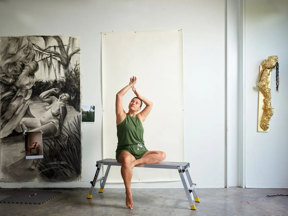 Portrait of Wanda Raimundi-Ortiz stretching in her studio surrounded by works in progress.