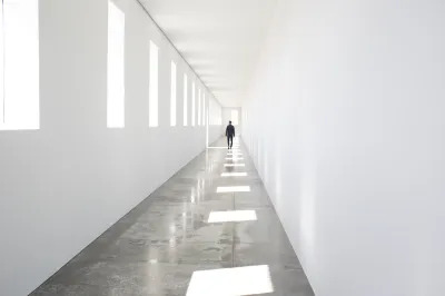 A person walking down a hallway whose walls have squares cut out of them. Light pours in, throwing squares onto the floor as well.