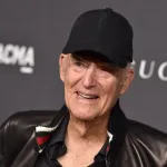 A smiling man wearing a black baseball cap and a leather jacket.