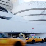 A spiraling museum building with taxi cabs rushing forward in front of it.