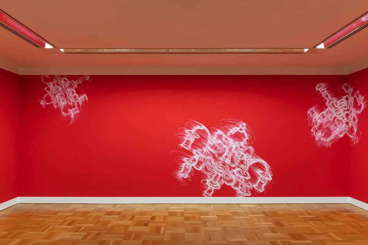 Partly erased chalk drawings of candelabras that float against a red wall.