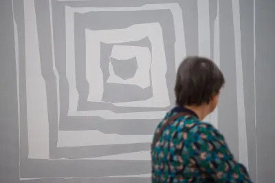 A person staring at a painting of grey squares within squares.