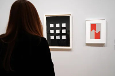 A woman staring at a drawing of rows of white squares against a black background. One square is greyed and thrown out of alignment.