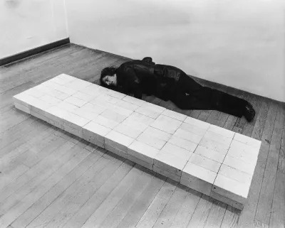 A man lying on the floor beside a sculpture formed from rows of bricks.