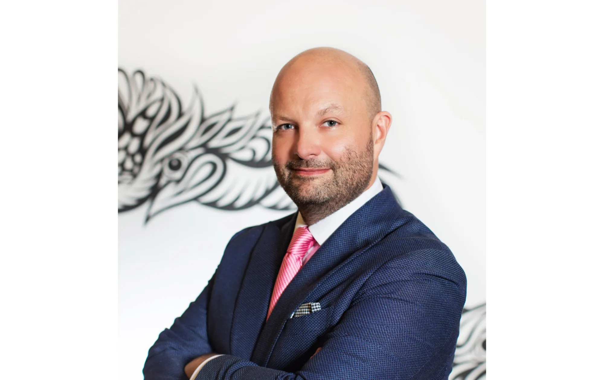A closely cropped profile photo of ART SG cofounder Magnus Renfrew. He is wearing a navy blue suit, a white dress shirt, a pink striped tie, and his arms are crossed.