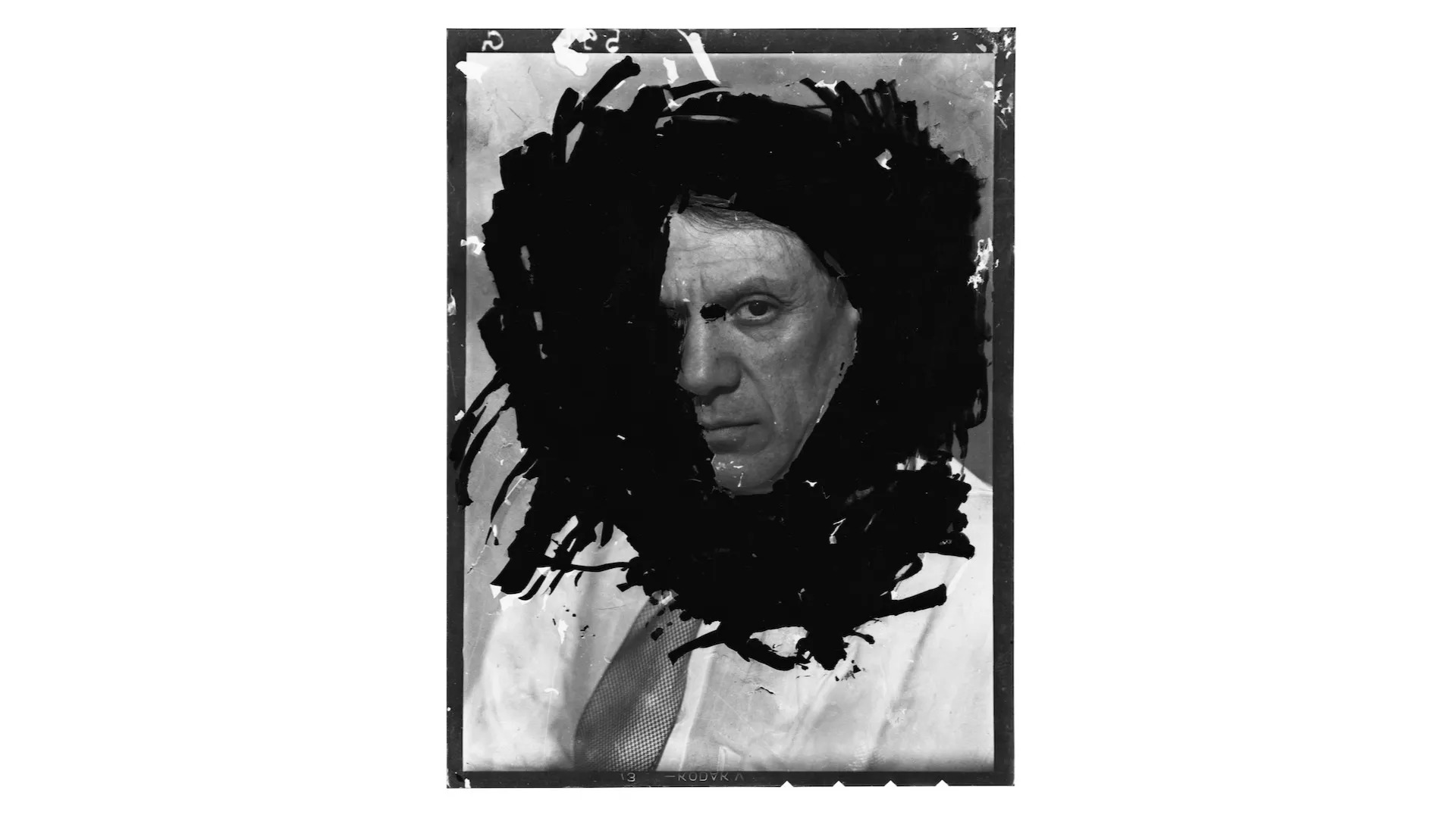 Portrait of Picasso with black marks surrounding his face so only one eye is visible.