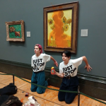 Two white protesters in tee shirts that say "just stop oil" have their hands glued to the wall in front of Van Gogh