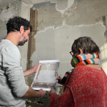 A man and a woman look at a printout of a newly discovered mural by Paul Cézanne while standing in front of that same mural.