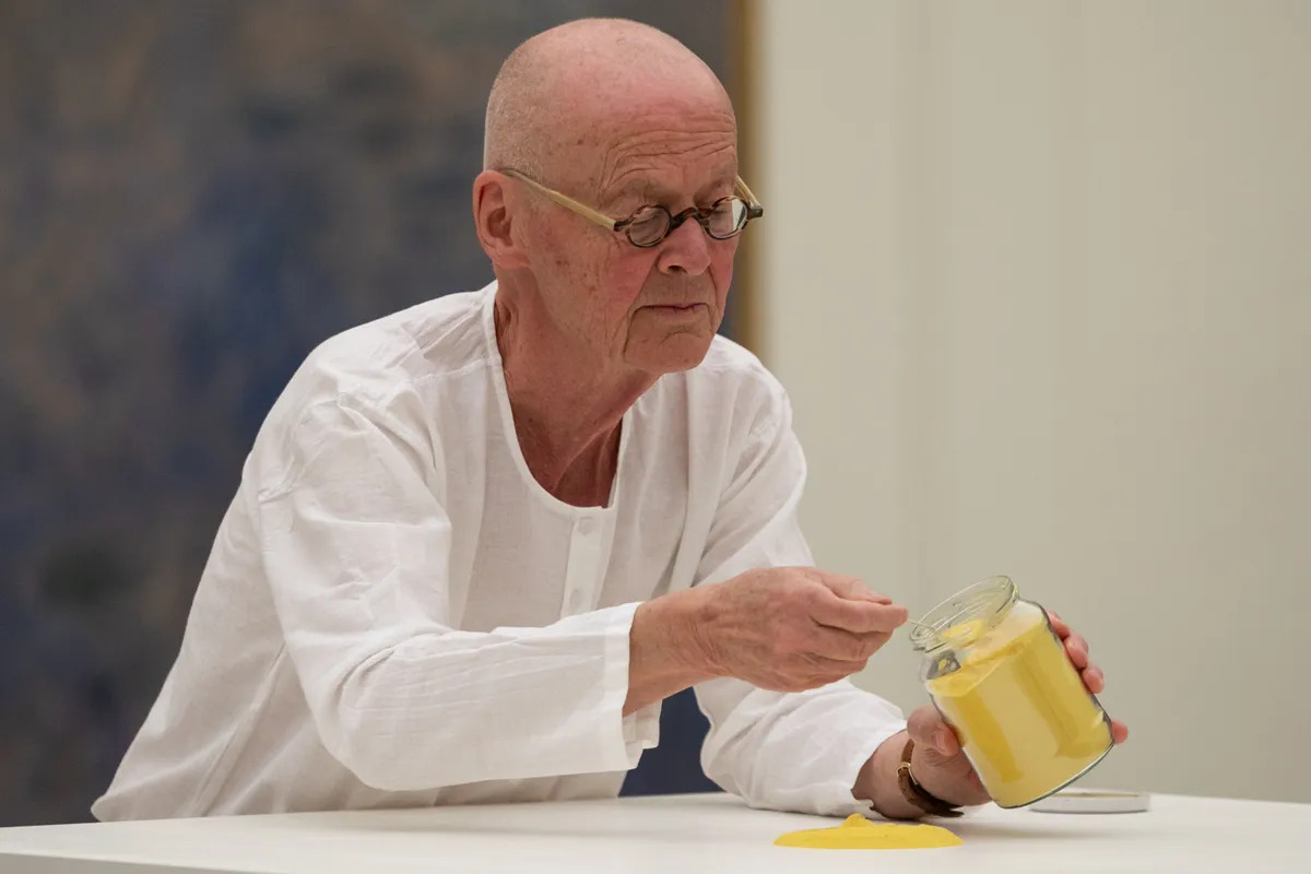 A man in a white collarless shirt places yellow pollen from a jar onto a plinth.