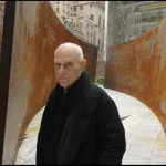 A white man standing amid a rusted steel sculpture.
