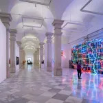 A long, columned hall with a glowing map of the United States facing an abstract painting.