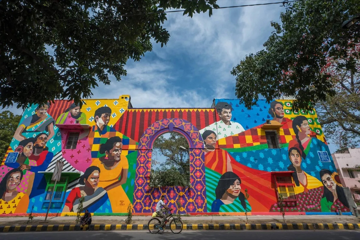 A building painted with a colorful mural of many different people interspersped with different patterns.