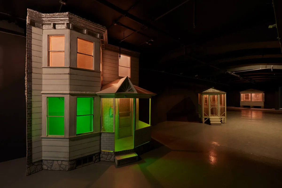 A sculpture of a two-story row house with a green light in the first floor.