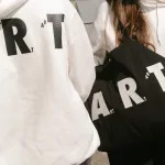 A white hoodie and a black tote bag printed with the word 