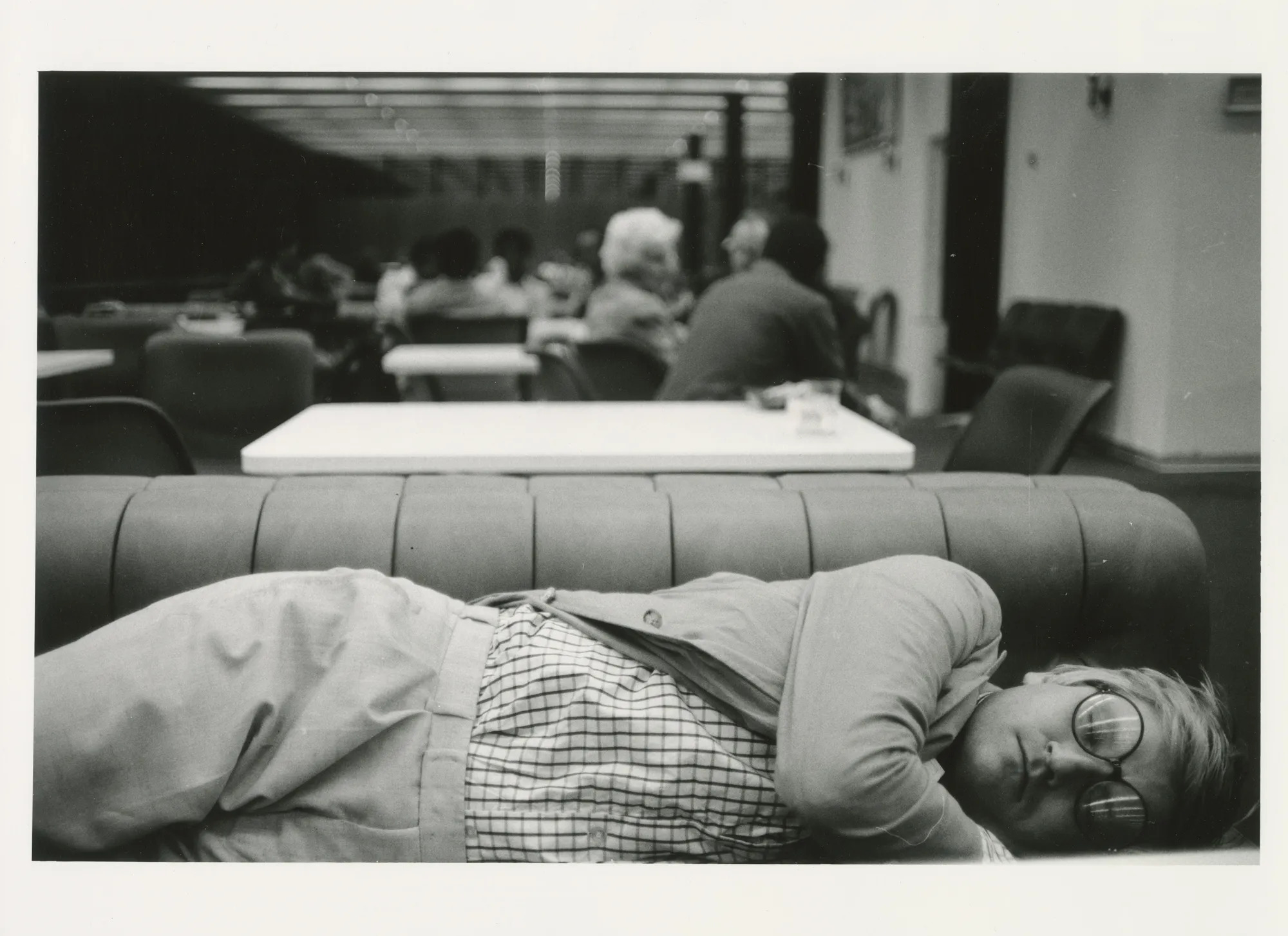 A man asleep in the transit lounge at an airport in a black-and-white photo.