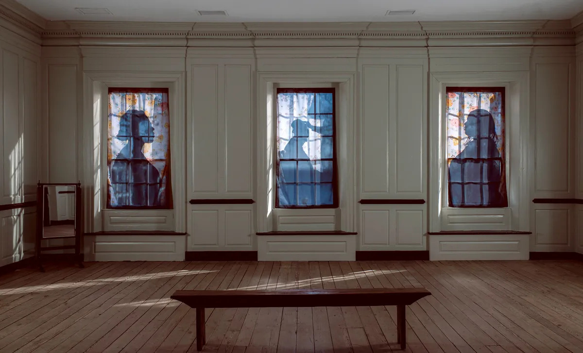 View of a courthouse in which three paned windows are covered by floral sheets that have silhouettes printed on them.