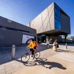 A student in a yellow jacket rides a bike in front of a building at the campus of Ringling College Art and Design, a private arts school in Sarasota, Florida. Ringling recently started offering a certificate in AI for its students.