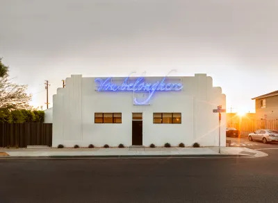 View of an art deco building that is painted white with a blue neon sign that reads 