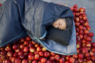 A Latina woman sleeping in a sleeping bag on top of apples.