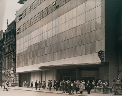 Archival black-and-white photograph of people gathering outside a museum building. There is a sign over a marquee that reads 