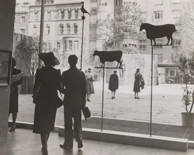 Archival black-and-white photo of people walking about a museum. 