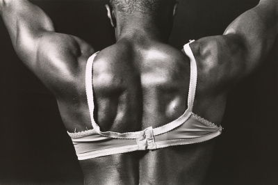 A muscular Black man wearing a white bra seen from behind.