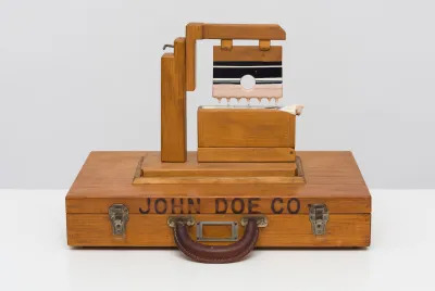 A wooden machine attached to a suitcase with the words 