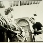 Archival photograph of a Filipino American man (right) talking in a classroom with a younger student who is a white woman and is looking at the man.