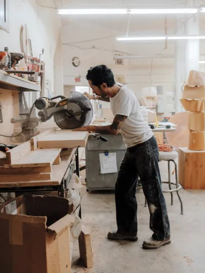 A man stands at workbench as he uses a miter saw on a fresh slab of wood. 