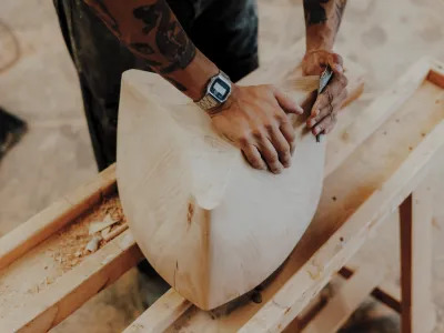 A close-up of a curved wood sculpture that a man is sanding down. 