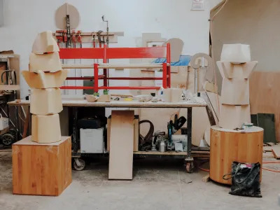 A red caned bench sits atop a work bench. There are several other in-progress wood sculptures nearby. 