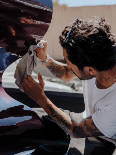 A man wipes a polished sculpture with a gray cloth. He is crouching in a truck bed. 