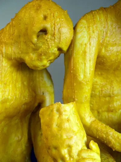 Two yellow sculptures of people, one leaning against the other