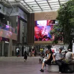 A mall atrium with people sitting on benches and walking on a staircase.