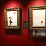 A woman looks at two paintings in a gallery with red walls.