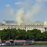 Smoke rising from the roof of a building near a river.