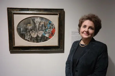 A white woman standing beside an abstract painting.