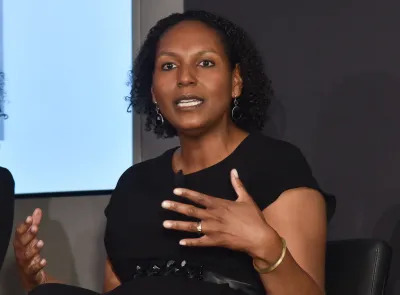 A Black woman speaking with her hands raised.