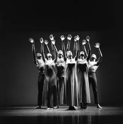 Archival photo of several dancers with their hands all raised as they look up. 