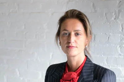 A white woman in a striped suit pictured against a white brick wall.