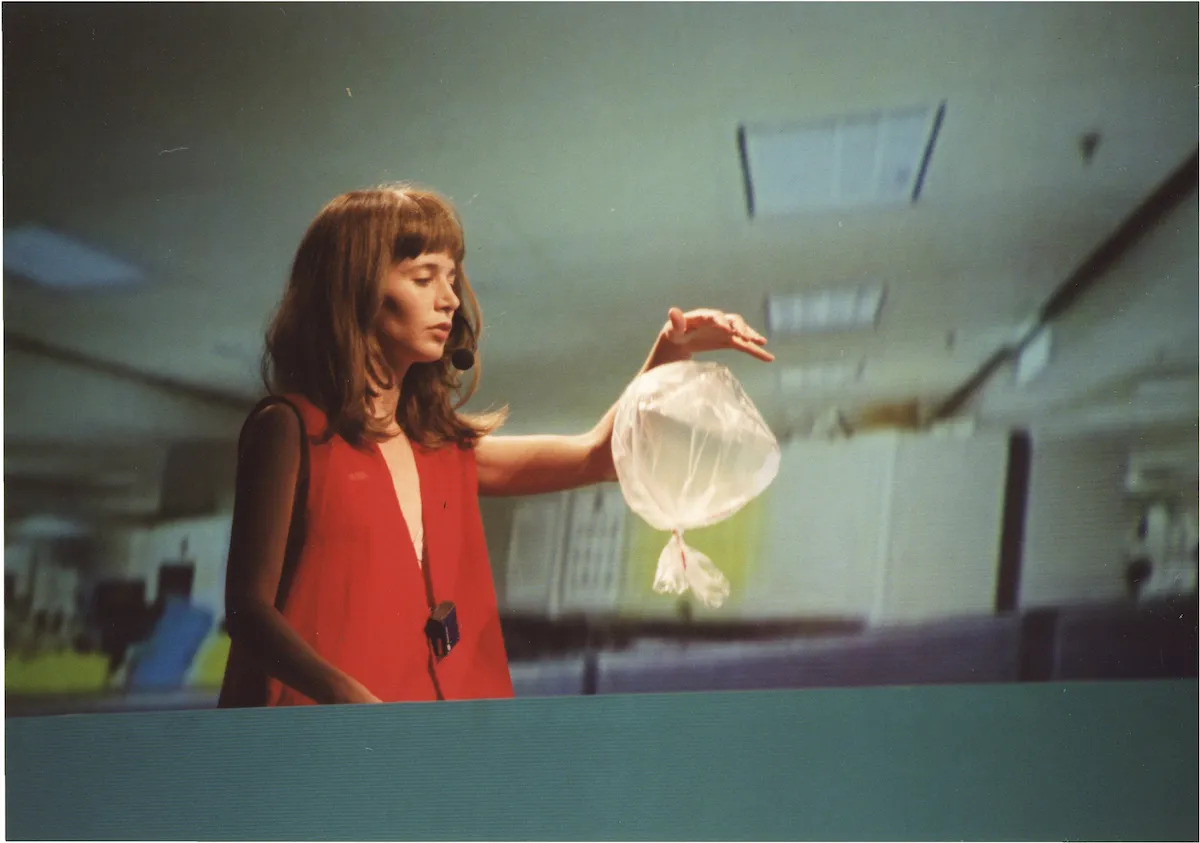 A woman in a red vest holds her hand out above a floating plastic bag.