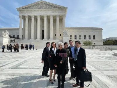 A group of people pose for a selfie being taken on an iPhone with a selfie stick in front of the US Supreme Court building. 