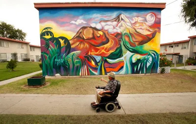 A 70-year-old man in his wheelchair glides past some of the murals he helped organize in 1973 that decorate the homes in Estrada Courts located at Olympic Blvd and Lorena street in the Boyle Heights neighborhood of Los Angeles on Monday June 24, 2013. Some of the murals painted 40 years ago have been repainted in an effort to preserve them. Since 2002 the City officially has imposed a ban on all mural painting on private buildings. Now, after years of lawsuits and negotiations the ban is likely to be lifted if City Council passes a new mural ordinance on tuesday.  (Photo by Al Seib/Los Angeles Times via Getty Images)