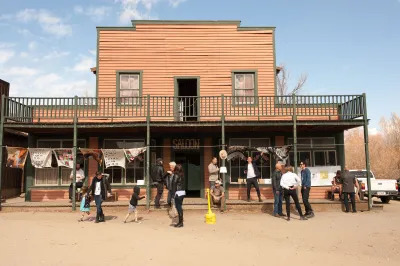 People walk by a two-story building in an old western town with the word 