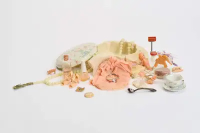 An opened box filled with an assortment of objects, including a ring, a toy spoon, a doll, a teacup, and more.