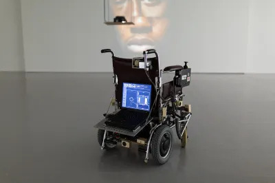 A wheelchair with a laptop attached to its back.