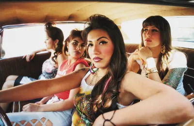 A group of women in a car, with the driver resting one arm on the window and one hand on the wheel.