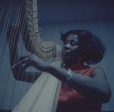 A Black woman strumming a harp.