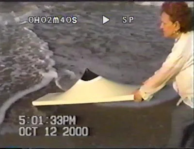 A woman putting a shaped canvas into the ocean.