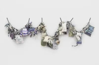 A wall-hung sculpture lined with bags containing toy jackets, shredded paper, and more.